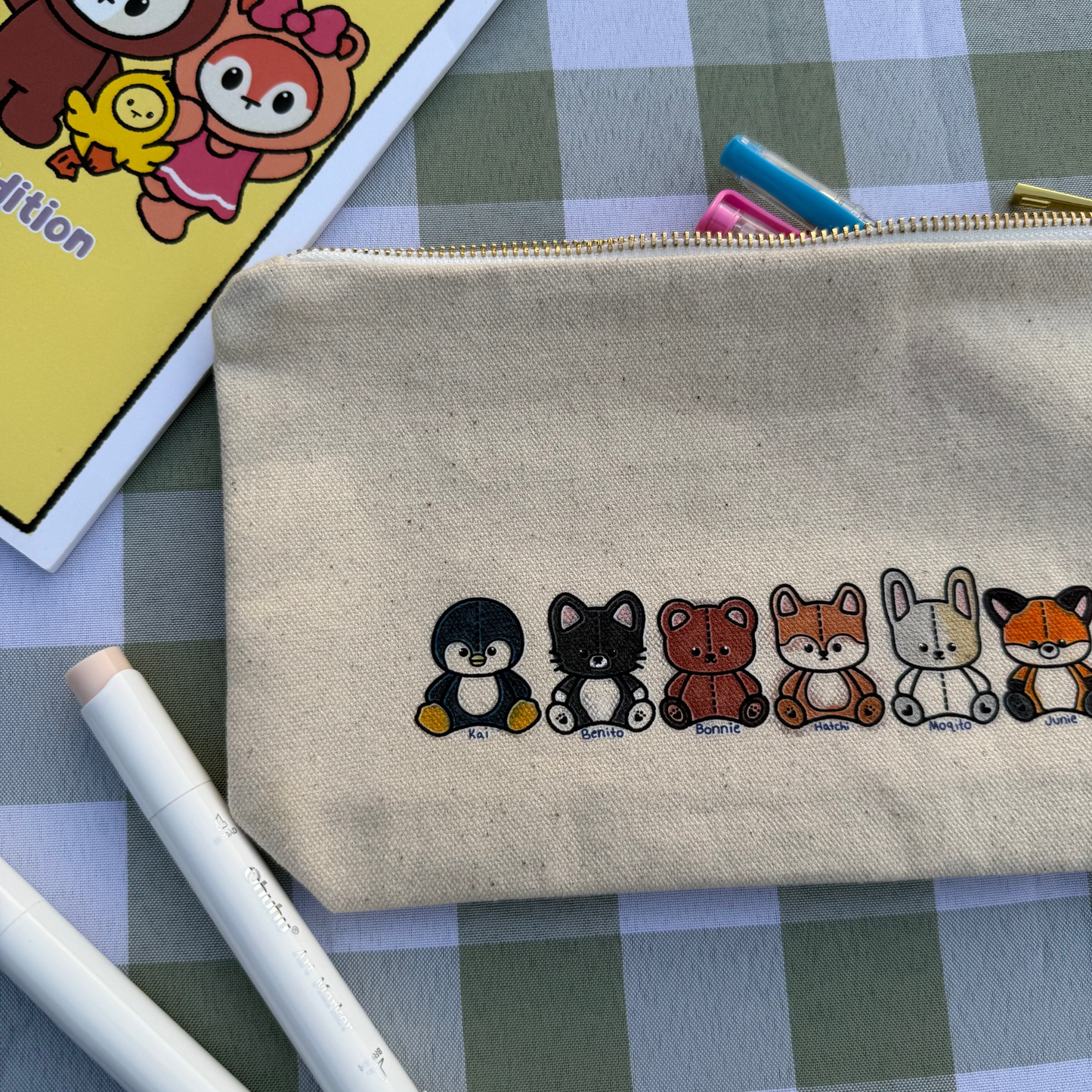 Beige pouch with cartoon bear designs on a checkered tablecloth with coloring books and markers.
